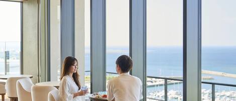 Un comedor moderno con amplios ventanales que dan a un puerto deportivo y al mar.