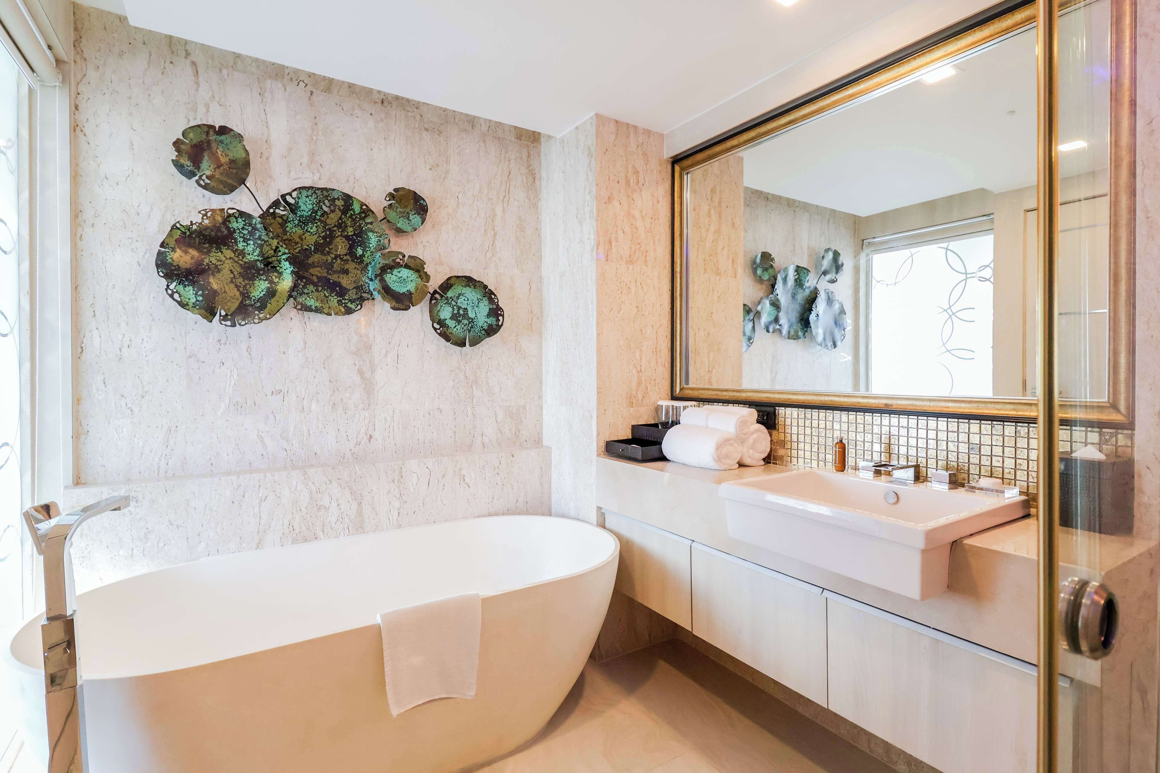 A modern bathroom with a freestanding bathtub, a large mirror, and decorative wall art.