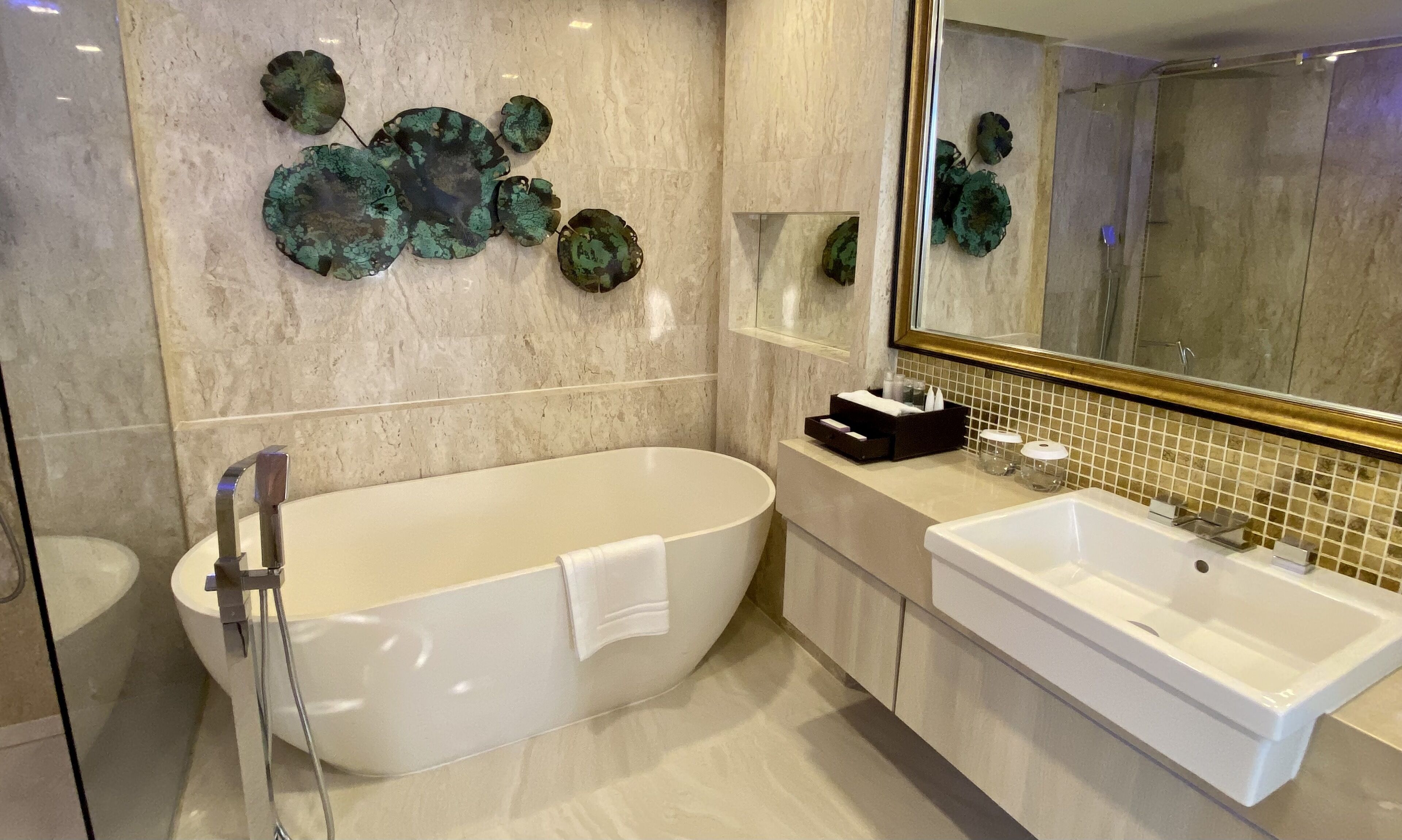 A modern bathroom with a freestanding bathtub, a large mirror, and decorative wall art.