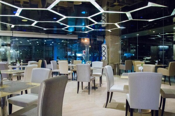 Un restaurant moderne doté de luminaires hexagonaux au plafond, de murs en verre et d’un intérieur épuré et contemporain.