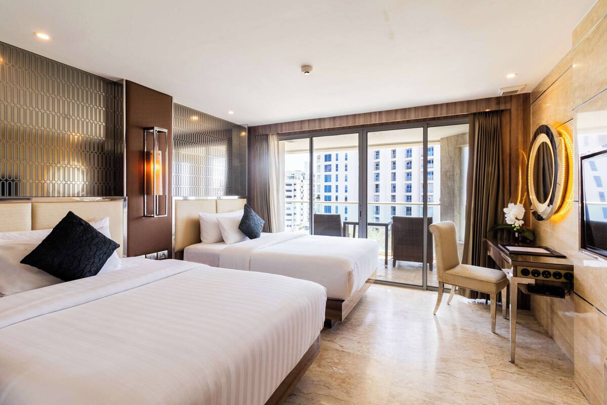 Hotelkamer met twee bedden, een bureau, een stoel, een televisie en grote ramen met uitzicht op de stad.