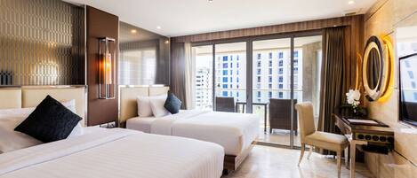 A hotel room with two beds, a desk, a chair, a TV, and large windows offering a city view.