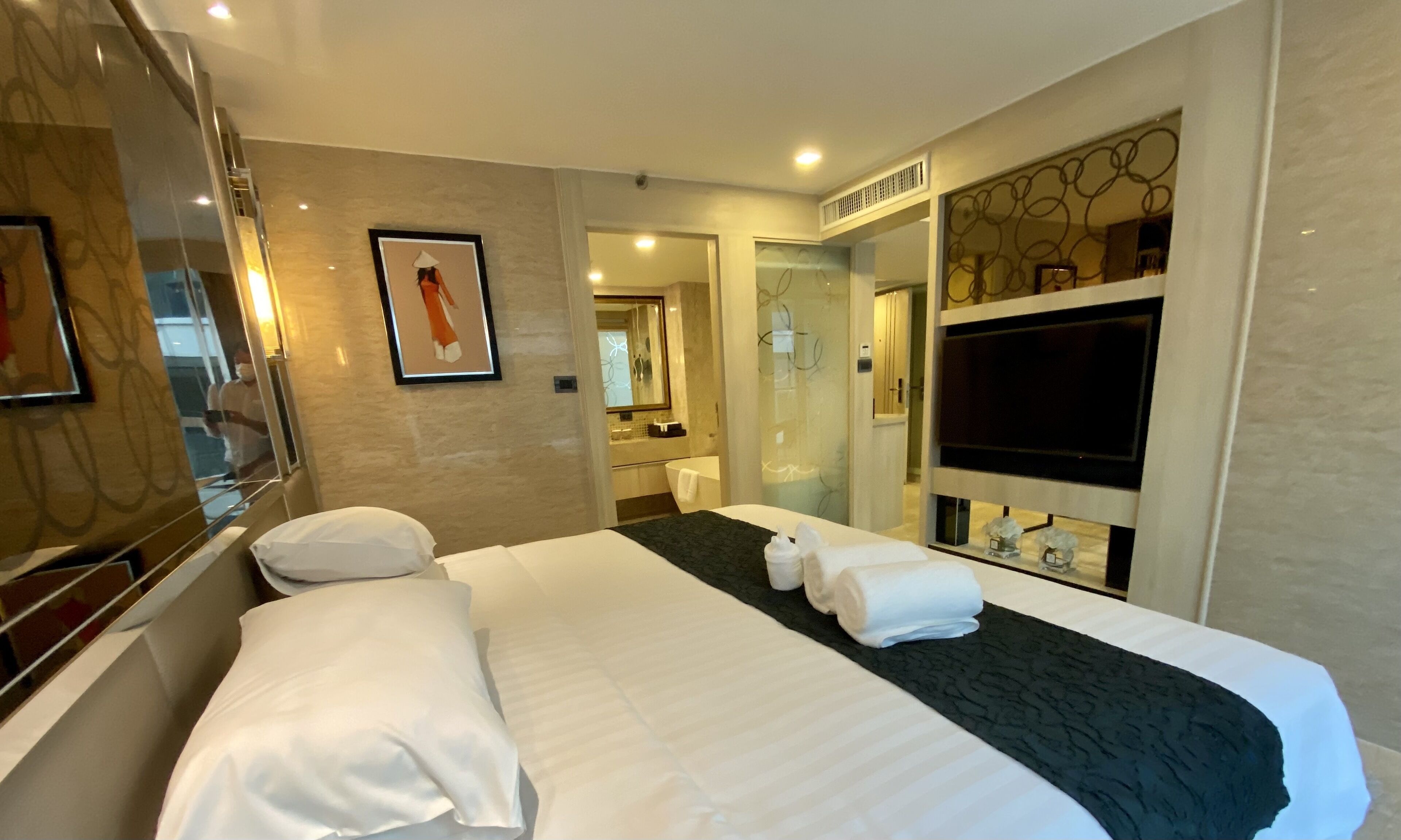 A hotel room with a large bed, a bathroom with a bathtub, and a TV mounted on the wall.