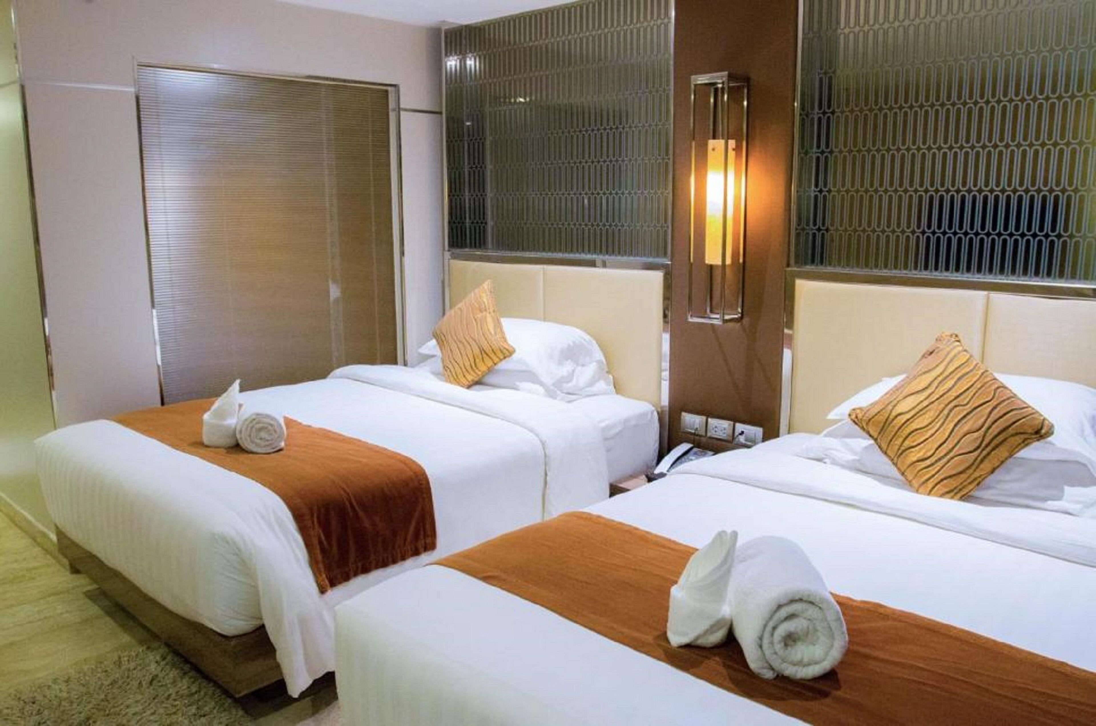 A hotel room with two beds, each with white linens and brown headboards. There are towels on the beds and a wall-mounted light fixture.