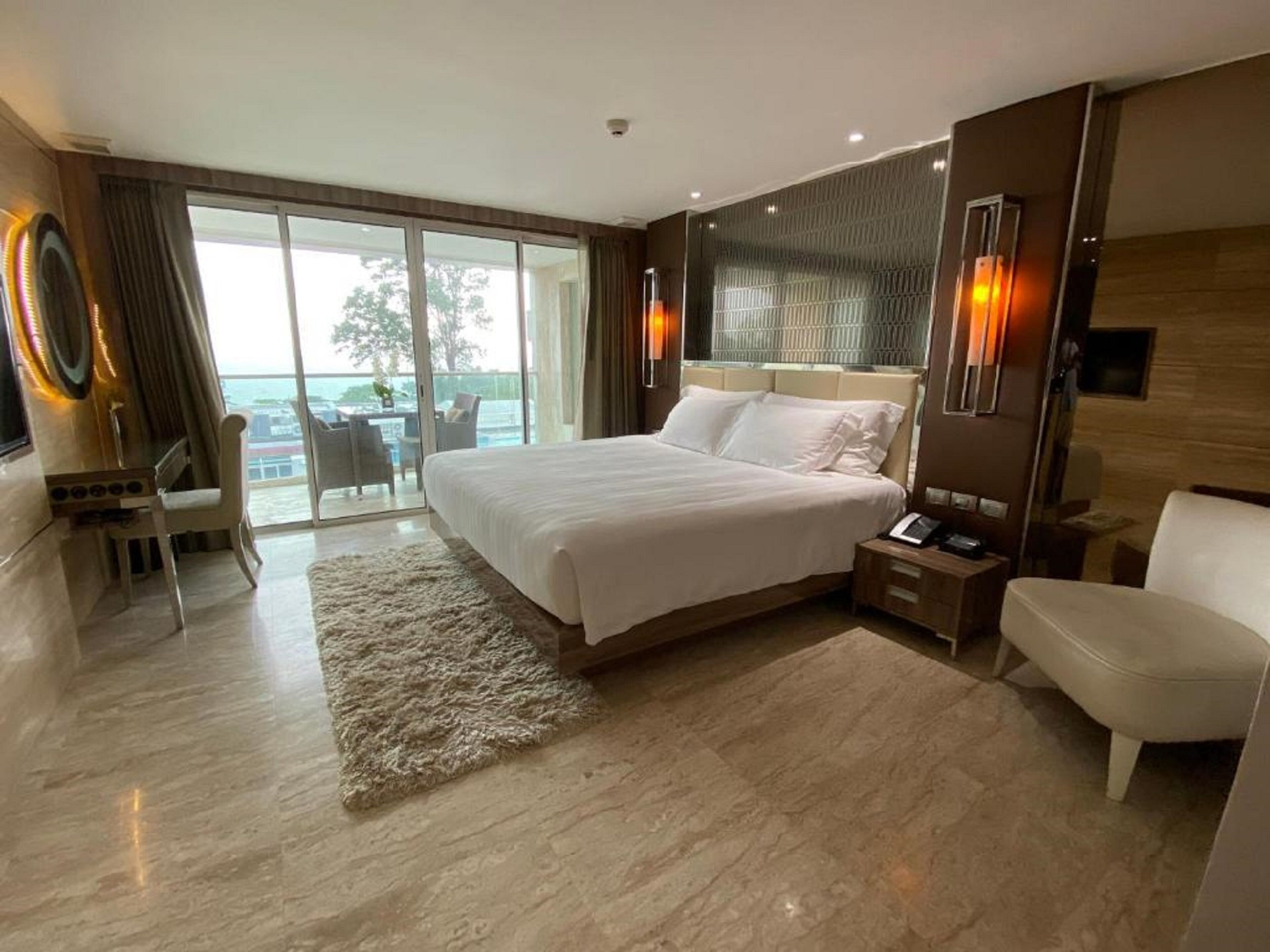Una camera d'albergo moderna con un letto grande, una scrivania e una sedia. Si vede l'oceano attraverso le porte scorrevoli in vetro.