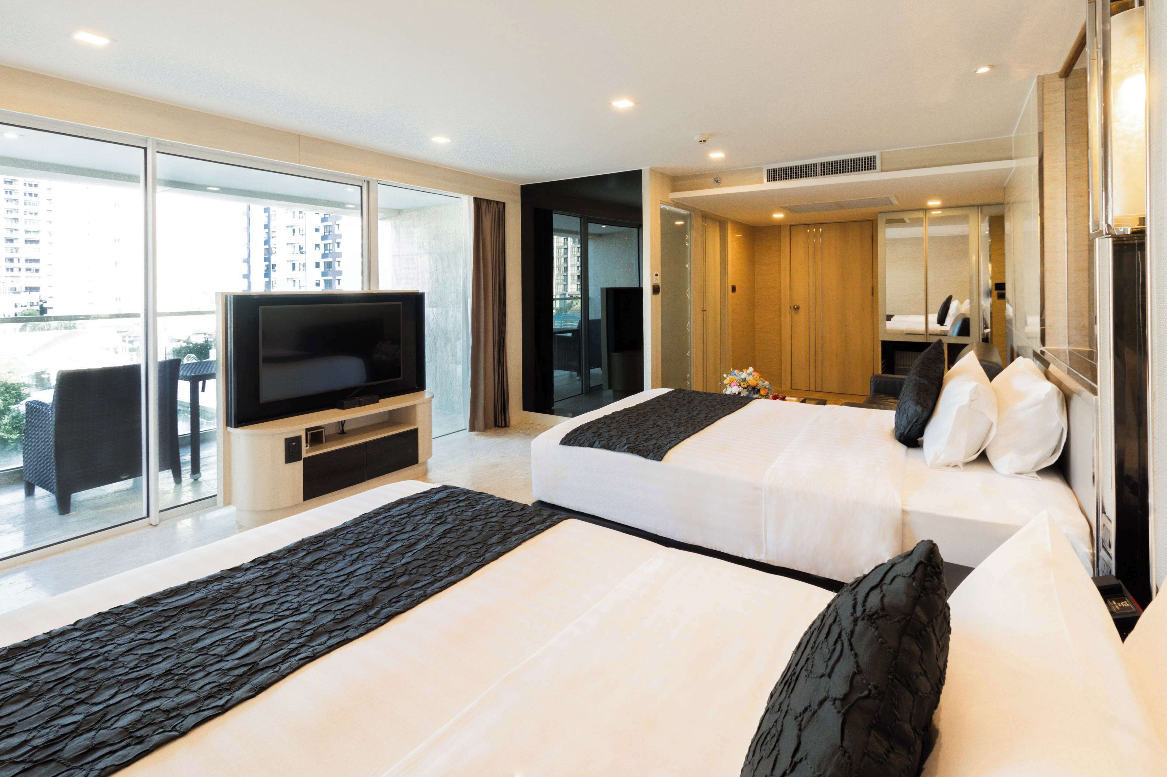 A modern hotel room with two beds, a TV, and a large window with a city view.