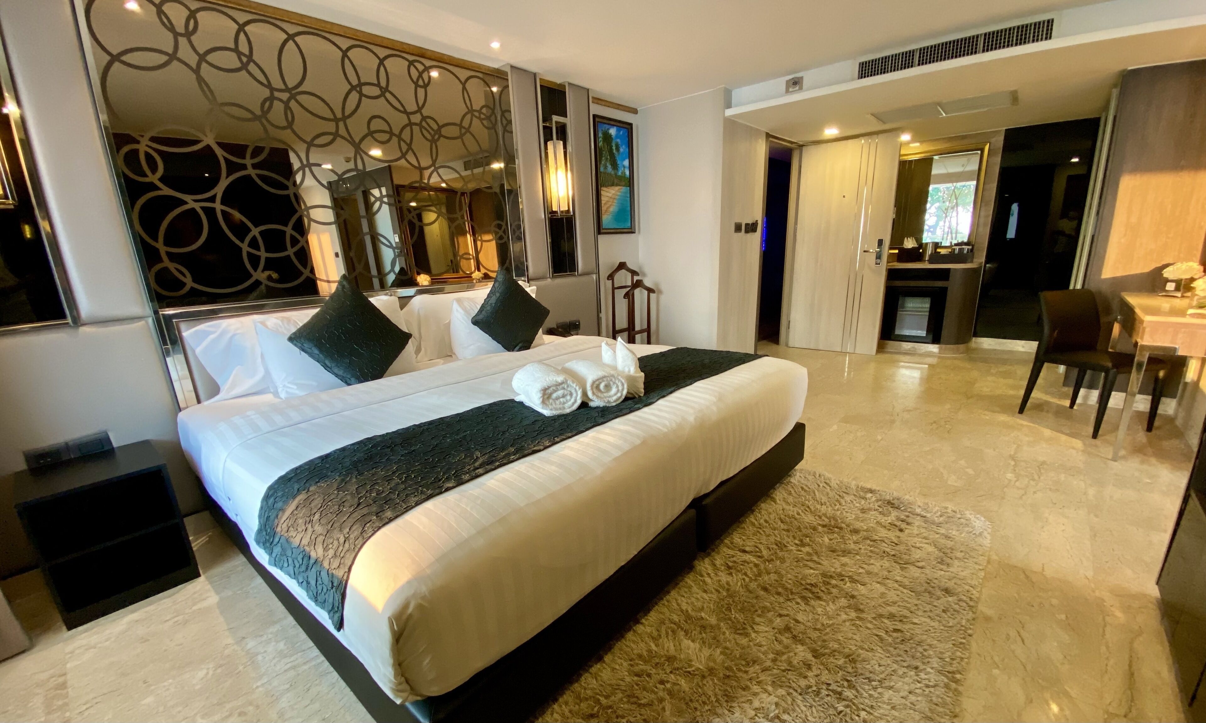Une chambre d’hôtel moderne, dotée d’un grand lit, d’un bureau et d’une salle de bain visible à travers une porte ouverte.