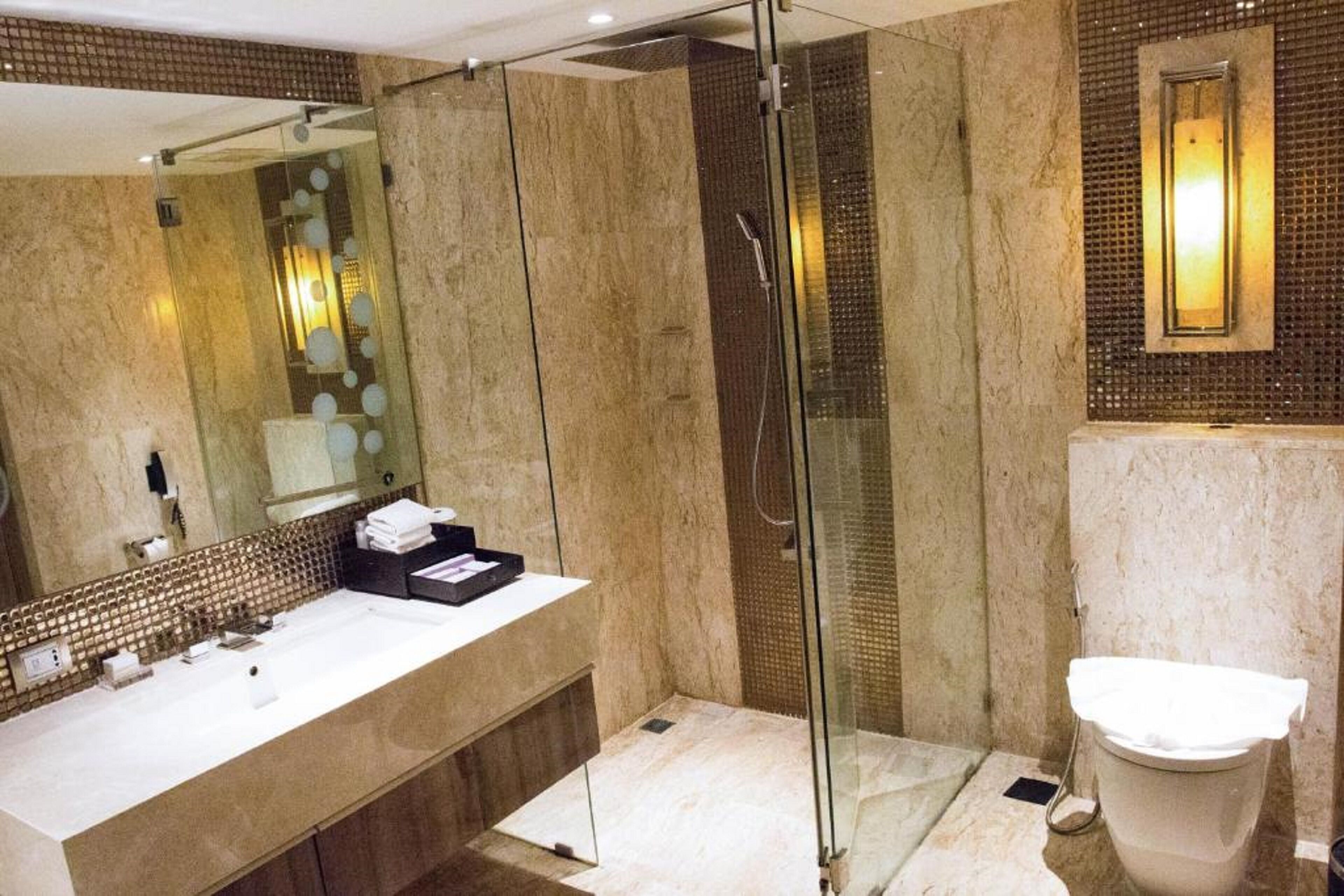 A modern bathroom with a glass-enclosed shower, a large mirror, and a marble countertop.