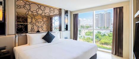 A modern hotel room with a large bed, a decorative wall panel, a nightstand, and a view of the city through large windows.