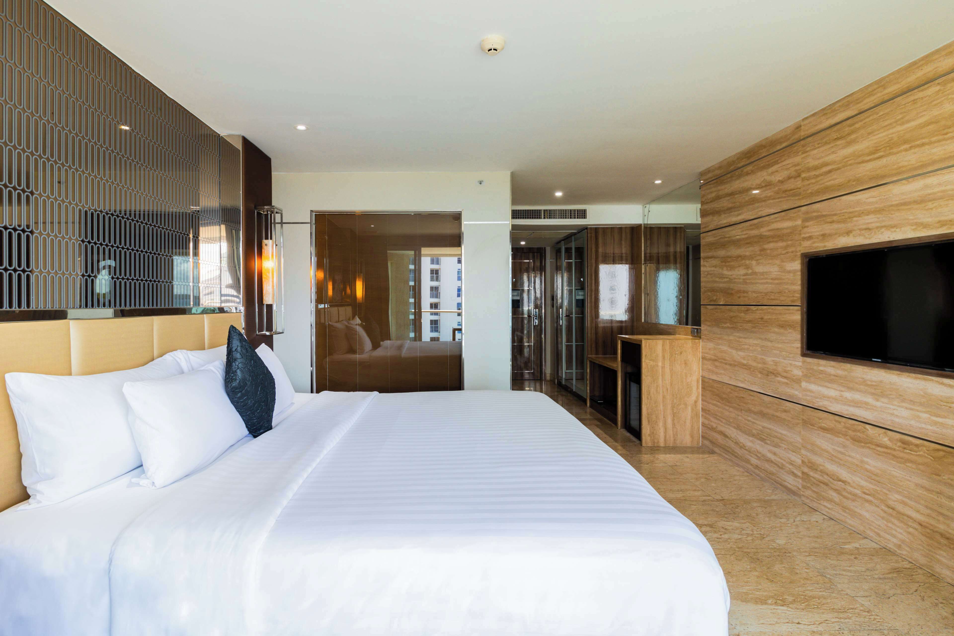 A modern hotel room with a large bed, a TV mounted on the wall, and a view of the city through the window.