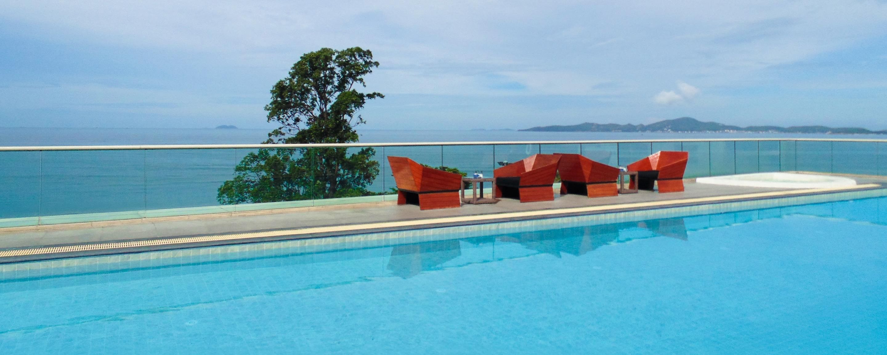 Un espace aménagé au bord de la piscine, offrant une vue sur la mer et les collines, avec un coin salon rouge et un panneau indiquant la certification GSTC.