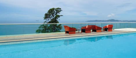 Zona junto a la piscina con vista al mar y colinas, que incluye un espacio de descanso rojo y un cartel que indica certificación GSTC.
