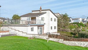 Une maison à deux étages dotée d’un balcon, d’un mur de soutènement en pierre et d’une pelouse bien entretenue.