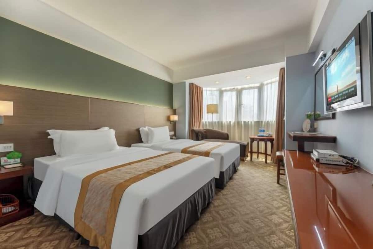 A hotel room with two beds, a desk, a chair, and a television.