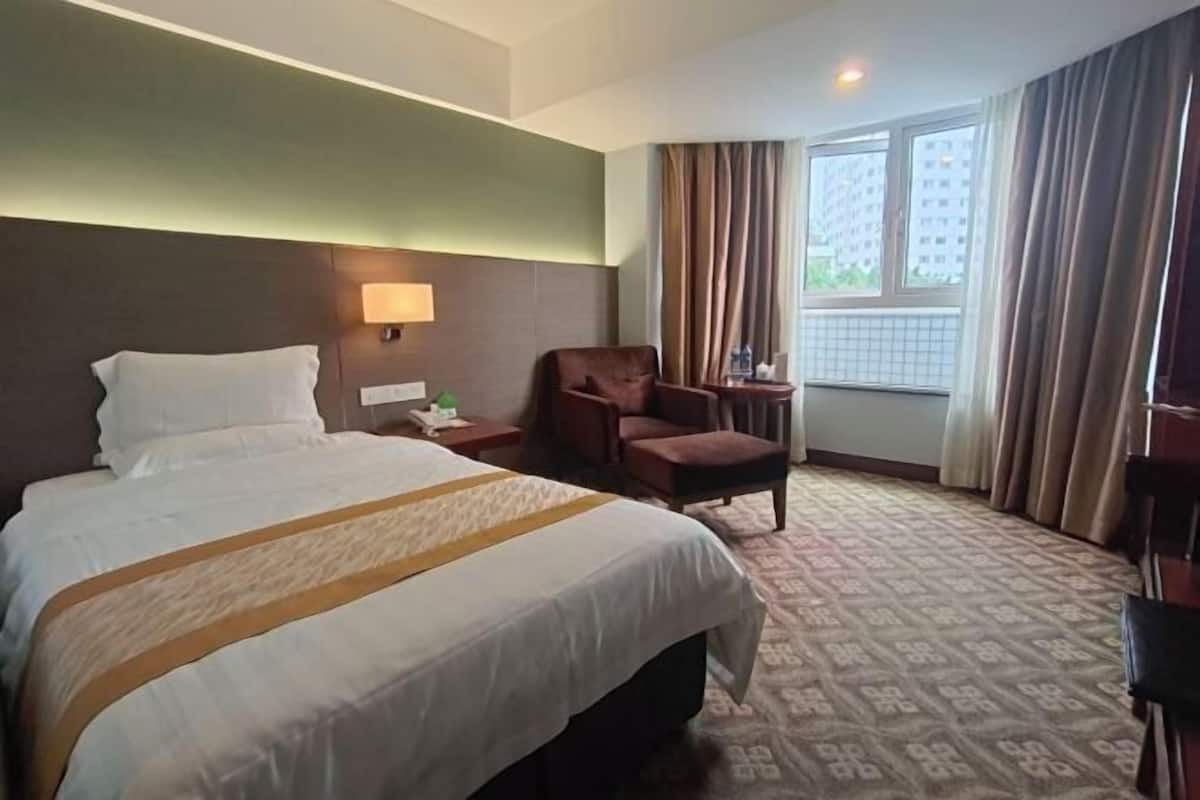 A hotel room with a large bed, a chair, a small table, and a window with curtains.