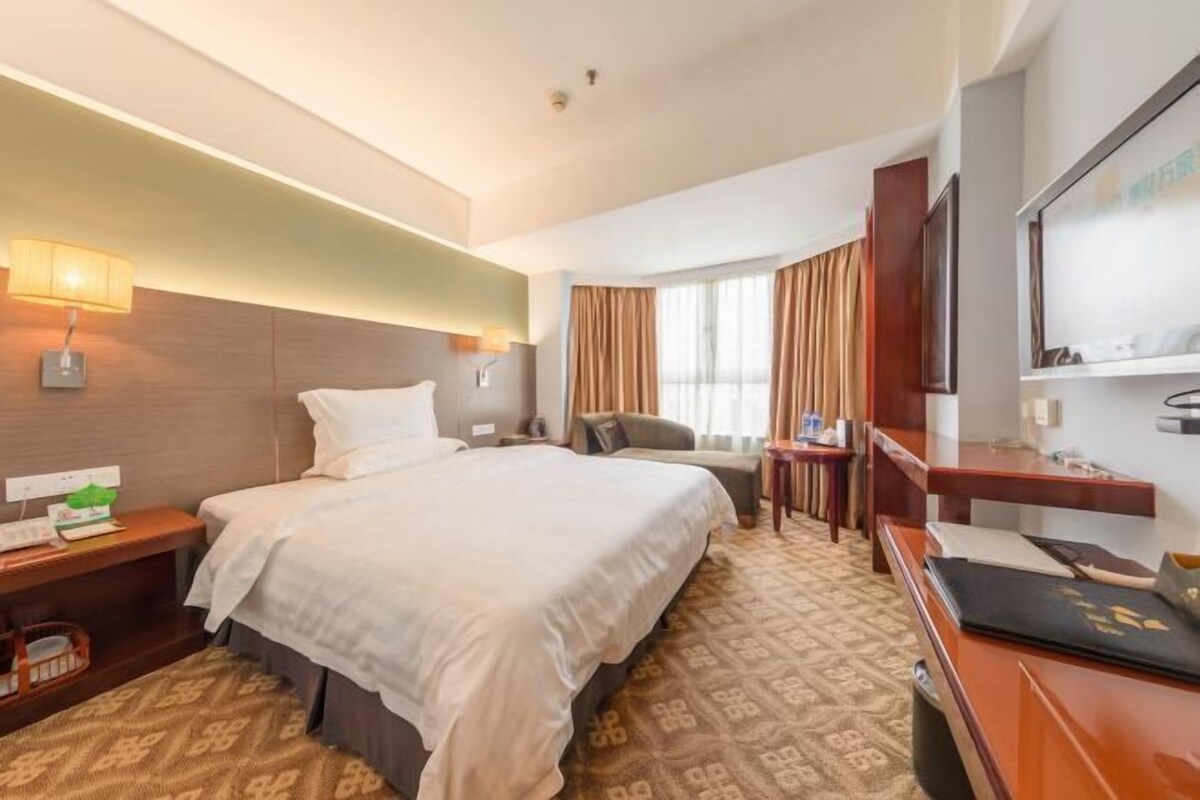 A hotel room with a large bed, a desk, a chair, a TV, and a window with curtains.