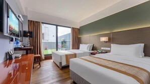 Quarto de hotel com duas camas, uma escrivaninha, televisão e uma janela grande.