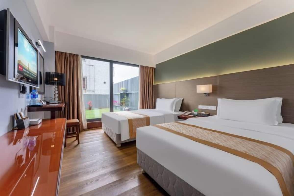 A hotel room with two beds, a desk, a TV, and a large window.