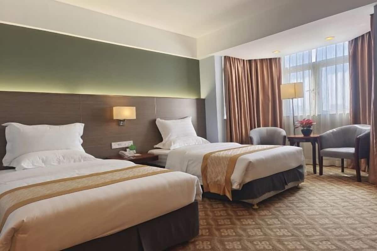 A hotel room with two beds, a small table, a chair, and a window with curtains.