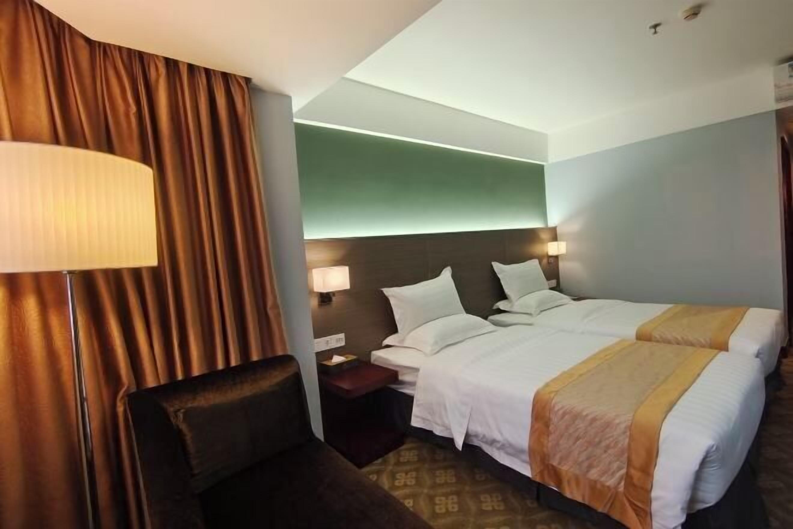 A hotel room with a double bed, two bedside tables with lamps, a chair, and a large window with curtains.