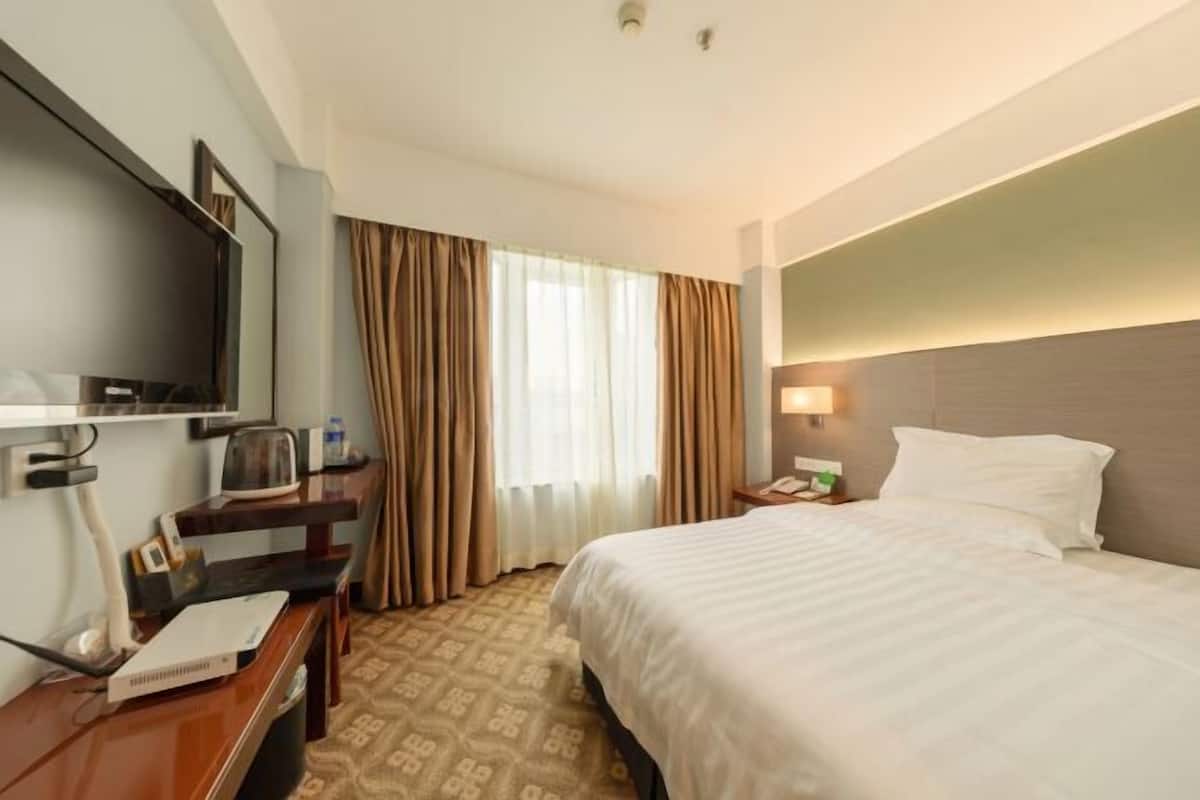 A hotel room with a bed, a desk with a computer, a TV, and a window with curtains.