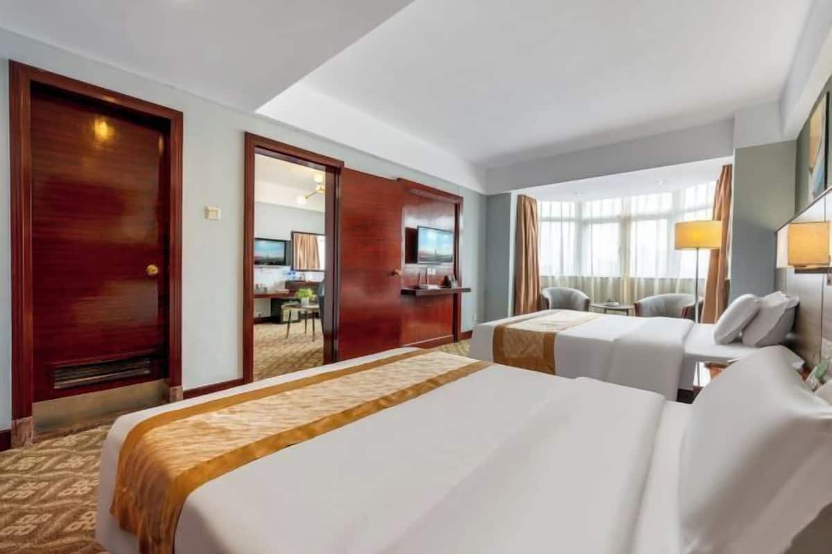 A hotel room with two beds, a desk, a chair, a TV, and a window with curtains.