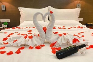 A bed with a heart-shaped towel arrangement and rose petals, a bottle, and a glass. - Shunjing Hotel (Zhongshan)