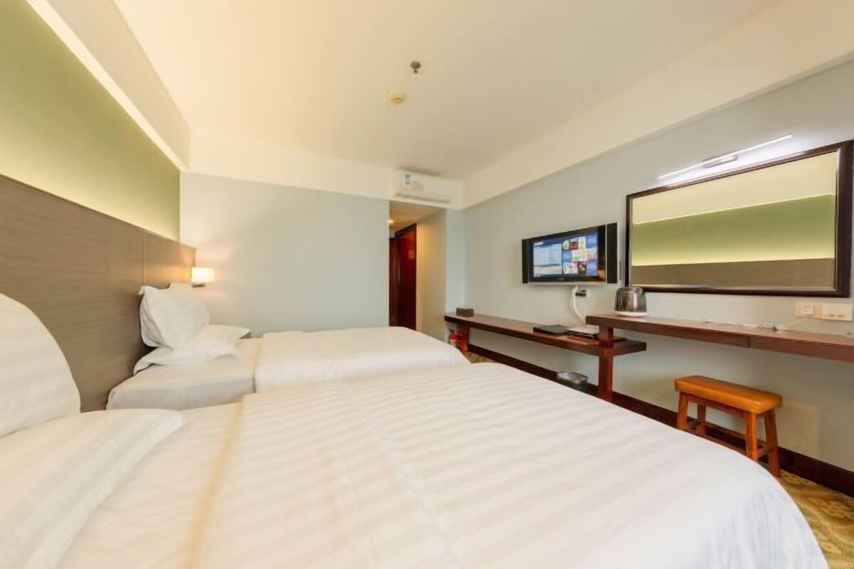 A hotel room with two beds, a desk, a chair, a television, and a large mirror.