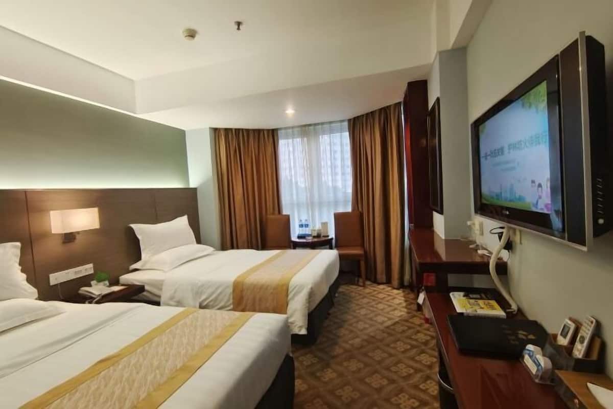 A hotel room with two beds, a desk with a television, and a window with curtains.