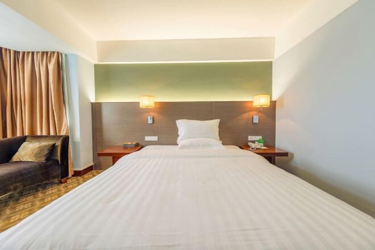 A hotel room with a large bed, two bedside tables, a sofa, and a headboard with wall-mounted lamps.