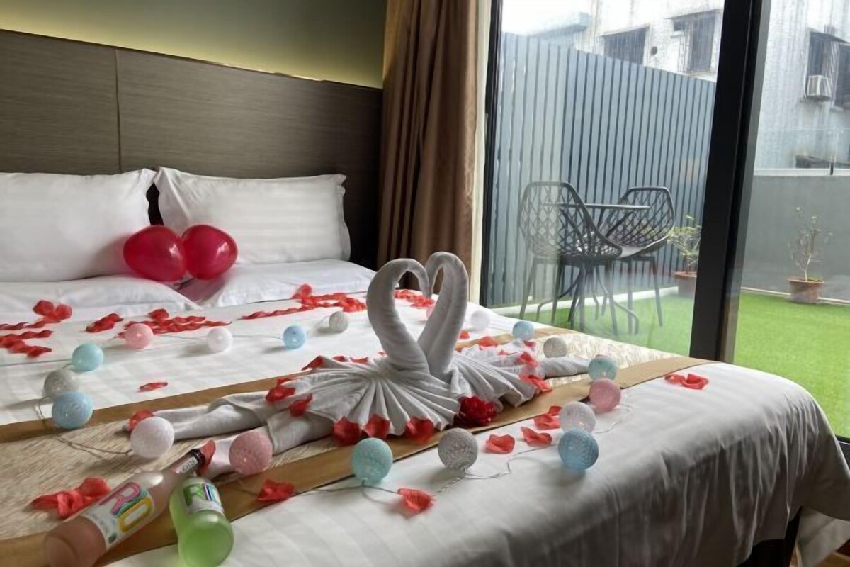 A hotel room with a bed, a swan-shaped centerpiece, balloons, and a view of the outside.