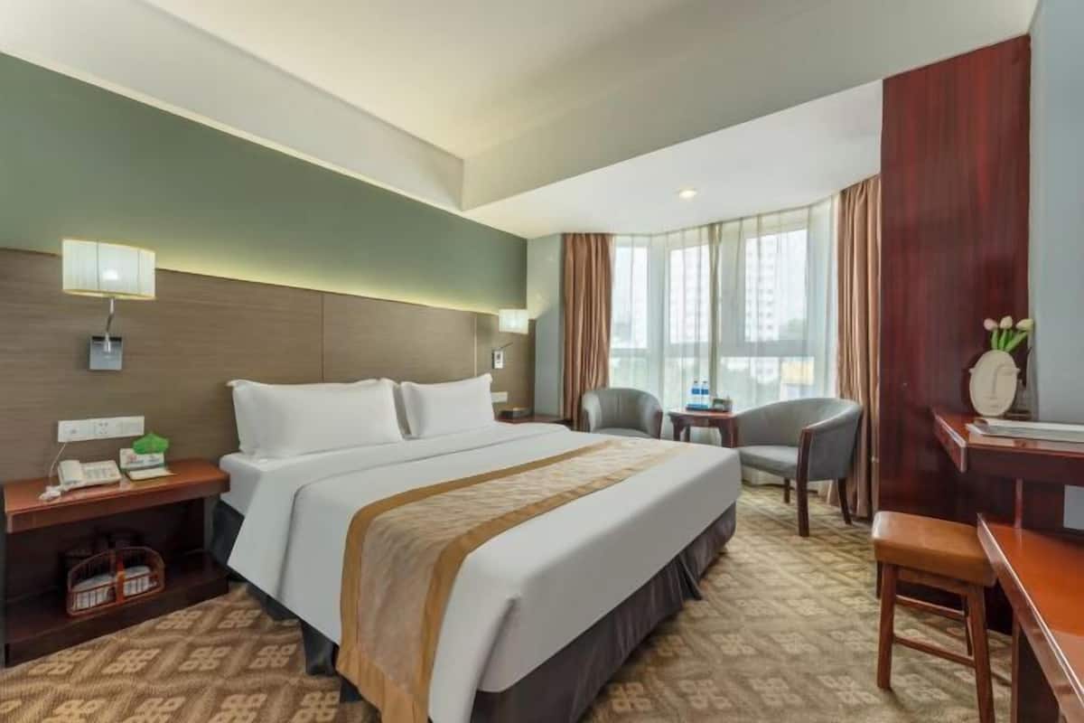 A hotel room with a large bed, a desk, a chair, a nightstand, and a window with curtains.