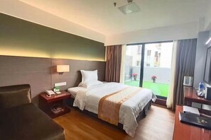 A hotel room with a bed, a desk, a chair, a nightstand, and a view of the outside.