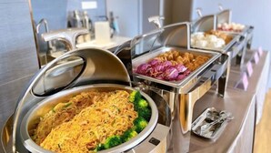 Buffet com diversas opções de comida, incluindo macarrão, legumes e outros pratos.
