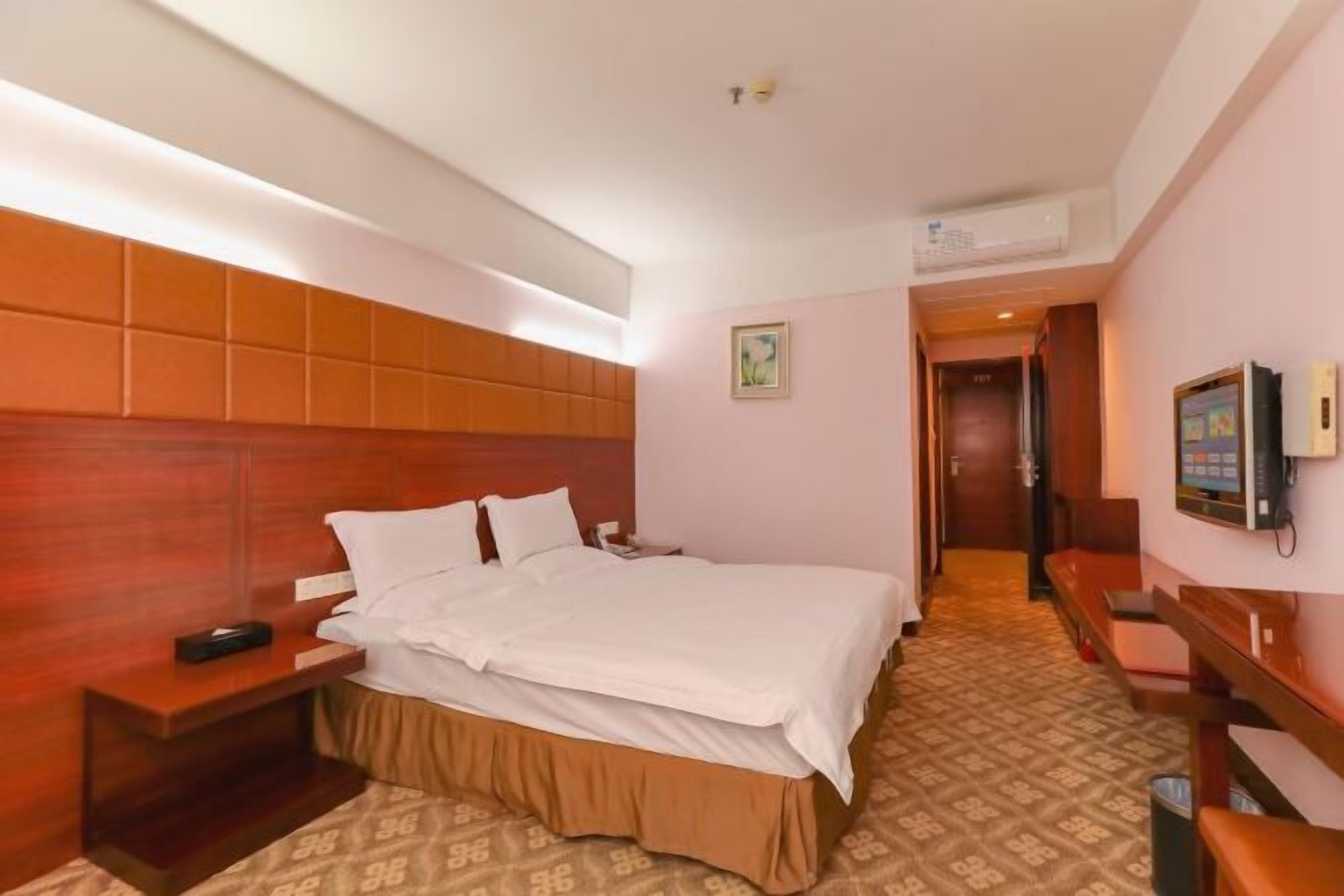 Una habitación de hotel con una cama grande, cabecera de madera, una mesita de noche y un televisor.