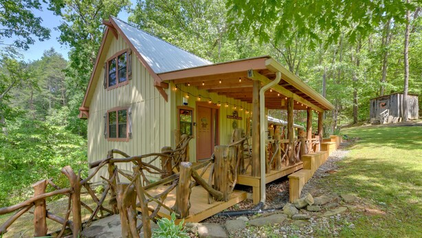 A rustic cabin with a wooden porch, surrounded by a natural forest setting.