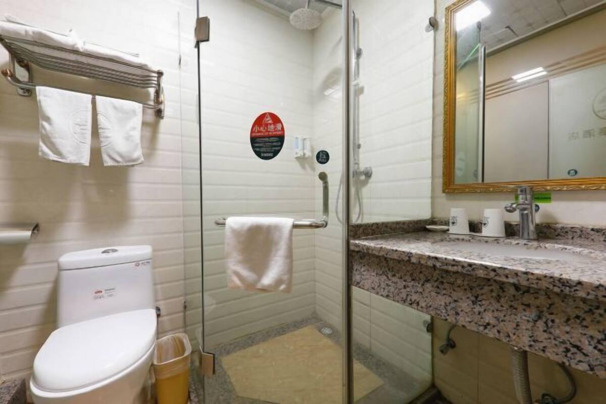 A bathroom with a toilet, a glass shower enclosure, a sink with a granite countertop, and a mirror with a gold frame.