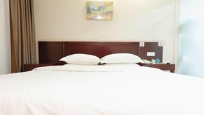 A neatly made bed with white linens and a wooden headboard, a painting on the wall, and a small table with a lamp beside the bed.