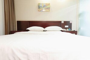 A neatly made bed with white linens and a wooden headboard, a painting on the wall, and a small table with a lamp beside the bed. - GreenTree Inn (Kunming South High-speed Railway Station Shilin Street) (Kunming)