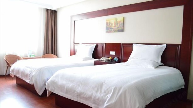 A hotel room with two single beds, a wooden headboard, a painting on the wall, and a chair.