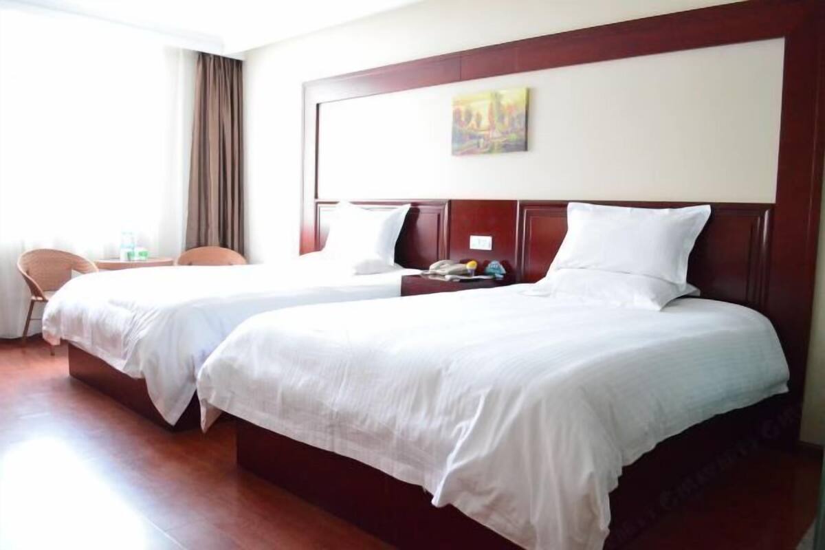 A hotel room with two single beds, a wooden headboard, a painting on the wall, and a chair.
