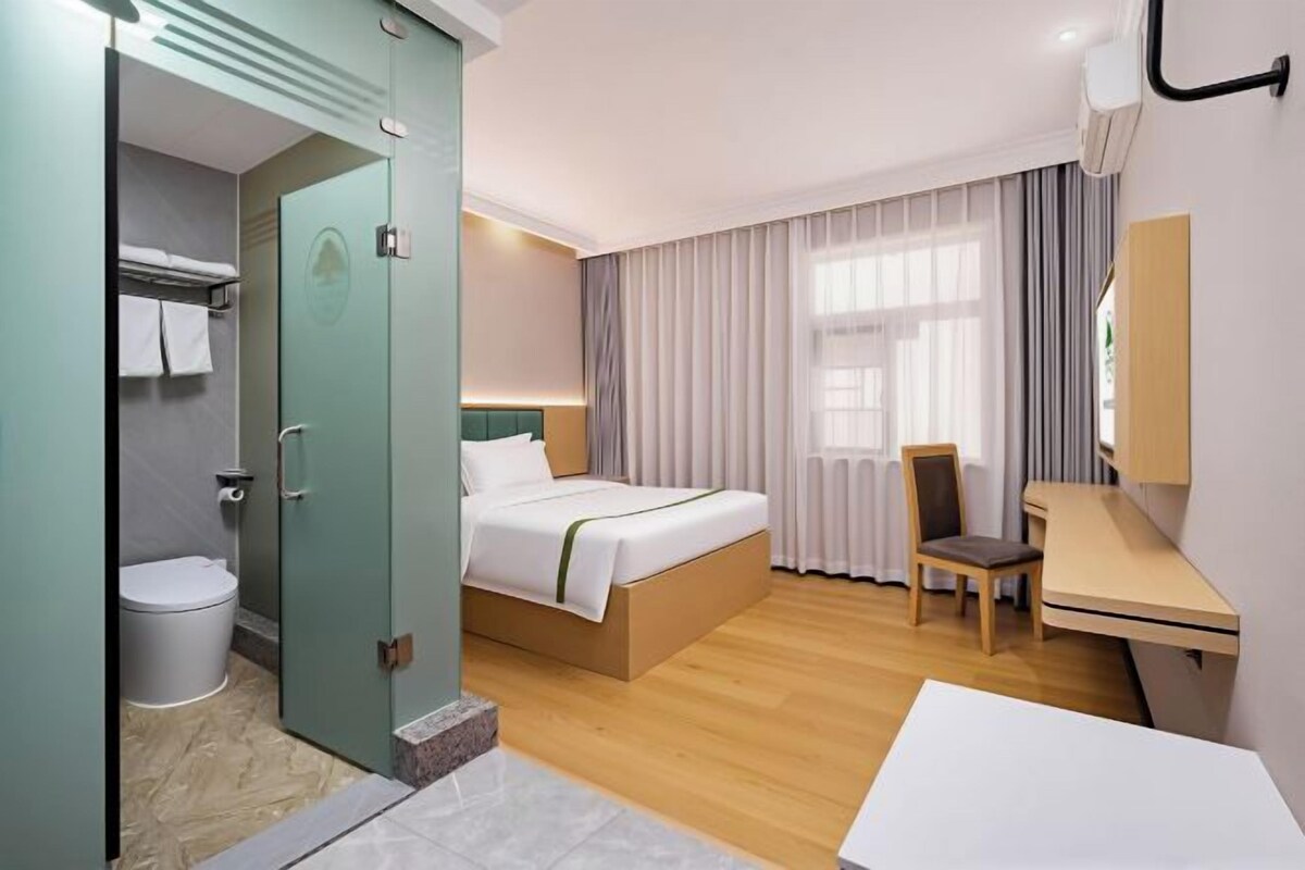 A hotel room with a bed, a desk, a chair, a toilet, and a shower area.