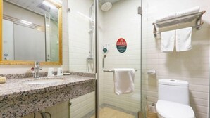 A bathroom with a glass shower enclosure, a sink with a granite countertop, a toilet, and a towel rack.