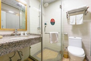 Uma casa de banho com cabine de chuveiro em vidro, lavatório com bancada de granito, sanita e porta-toalhas.