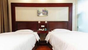 A hotel room with two beds, a wooden headboard, a small table with a telephone, and a painting on the wall.