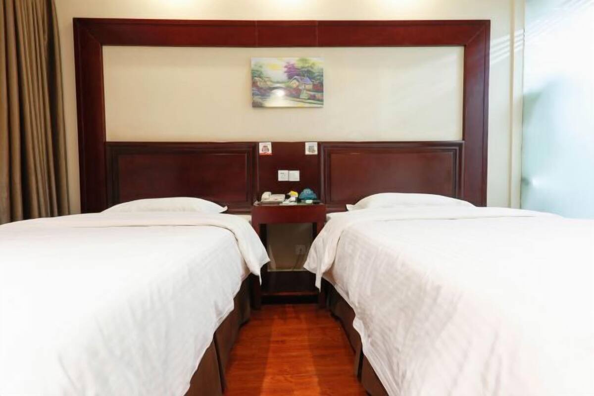 A hotel room with two beds, a wooden headboard, a small table with a telephone, and a painting on the wall.