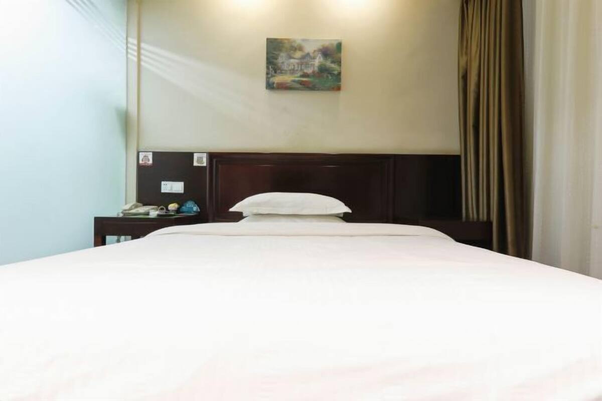 A hotel room with a bed, a nightstand, a painting on the wall, and a curtain.