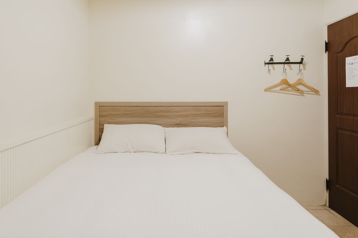 A single bed with a wooden headboard, white bedding, and a wooden door with a handle.