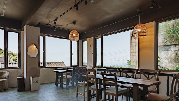 A spacious dining area with wooden tables and chairs, large windows, and hanging wicker lamps. - Mountain Traveler Inn (New Taipei City)
