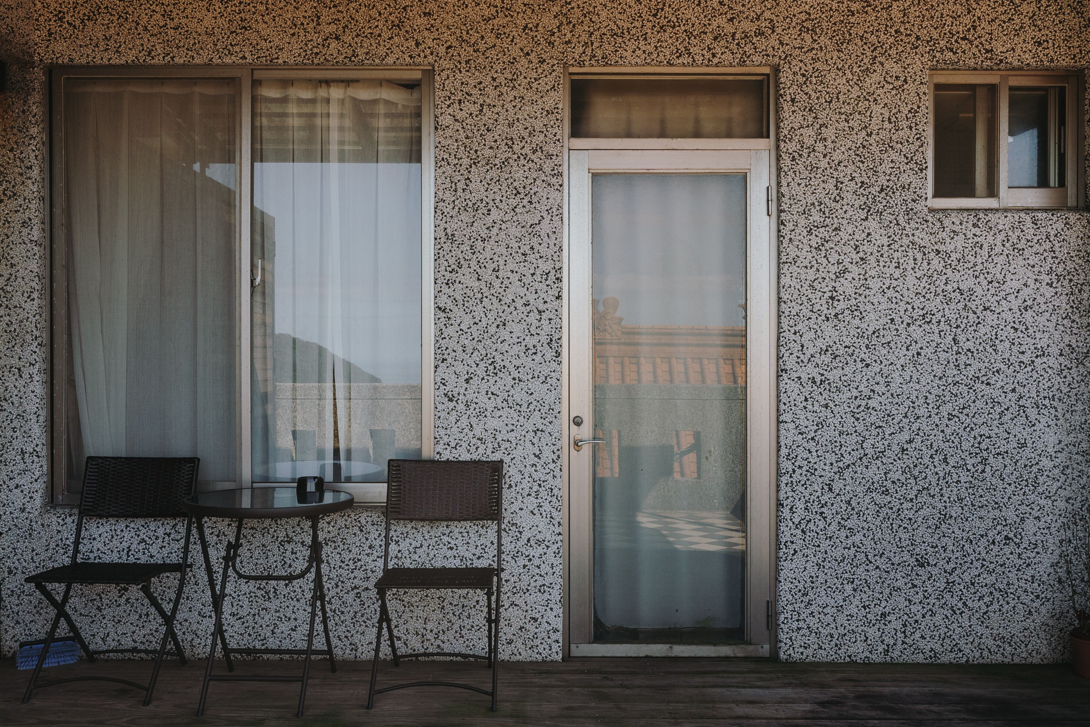 Une pièce avec une petite table et deux chaises, une porte dotée d’un panneau en verre dépoli et un mur à texture.